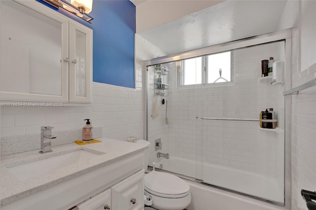 full bathroom featuring vanity, backsplash, toilet, and bath / shower combo with glass door