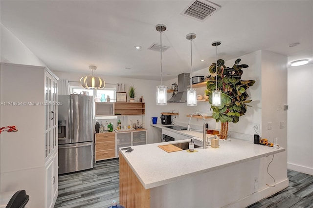 kitchen featuring kitchen peninsula, stainless steel fridge with ice dispenser, wall chimney exhaust hood, and hardwood / wood-style flooring