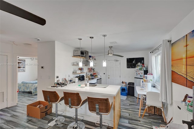 kitchen featuring ceiling fan, kitchen peninsula, decorative light fixtures, a breakfast bar, and hardwood / wood-style flooring