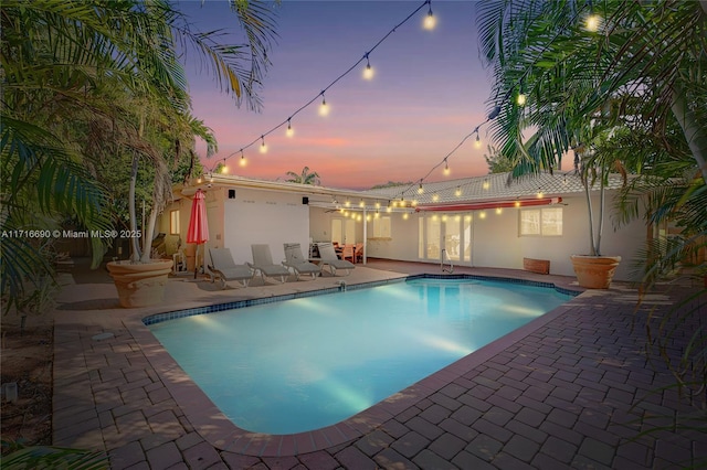 pool at dusk with ceiling fan and a patio area