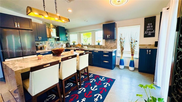 kitchen featuring light stone countertops, pendant lighting, wall chimney range hood, decorative backsplash, and a kitchen island