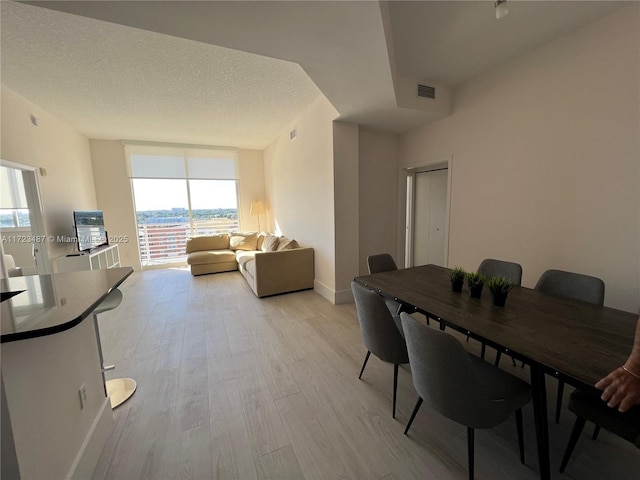 dining room featuring a textured ceiling, light wood-type flooring, and a wall of windows