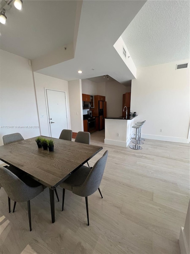 dining area with a textured ceiling, light hardwood / wood-style flooring, and sink