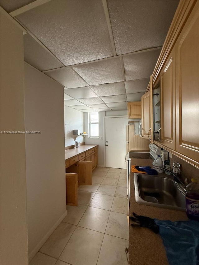 interior space with a drop ceiling, light brown cabinets, sink, light tile patterned floors, and range