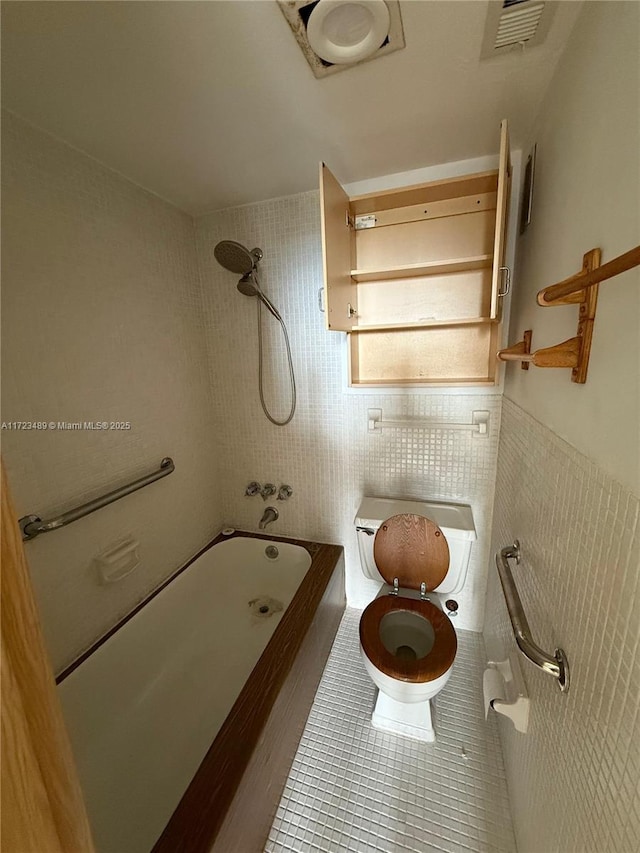 bathroom with tile patterned floors, tile walls, tiled shower / bath combo, and toilet