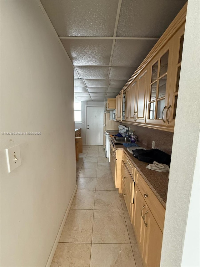 kitchen featuring light tile patterned floors, a paneled ceiling, dark stone countertops, and sink