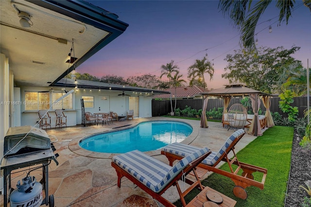 pool at dusk featuring a gazebo, grilling area, and a patio area