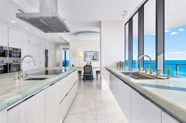 kitchen with island range hood, white cabinetry, a water view, and sink