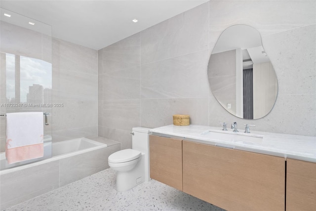 bathroom featuring vanity, toilet, tile walls, and tiled tub