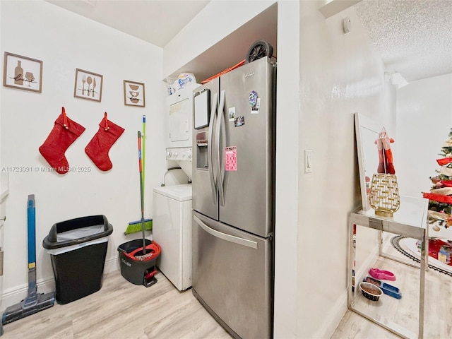 laundry room featuring a textured ceiling, light wood-type flooring, and stacked washer / dryer