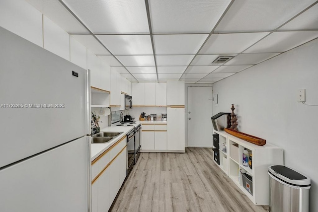 kitchen with a drop ceiling, sink, black appliances, white cabinets, and light hardwood / wood-style floors