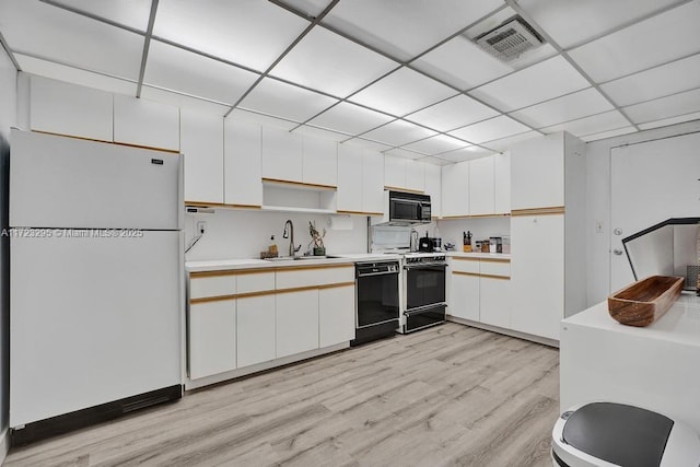 kitchen with a paneled ceiling, white cabinetry, sink, and black appliances