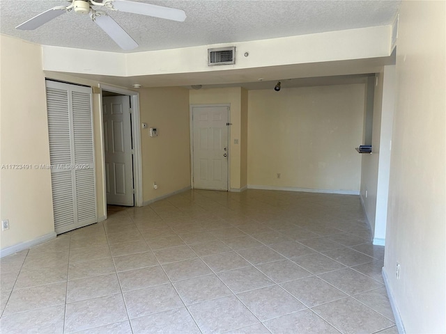 empty room featuring ceiling fan, light tile patterned floors, and a textured ceiling