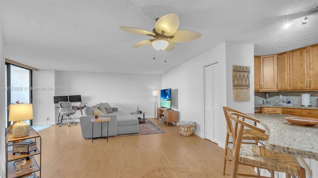 living room with light wood-type flooring, ceiling fan, and a textured ceiling