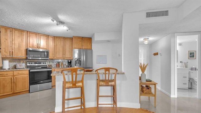 kitchen featuring tasteful backsplash, visible vents, a breakfast bar area, appliances with stainless steel finishes, and a textured ceiling