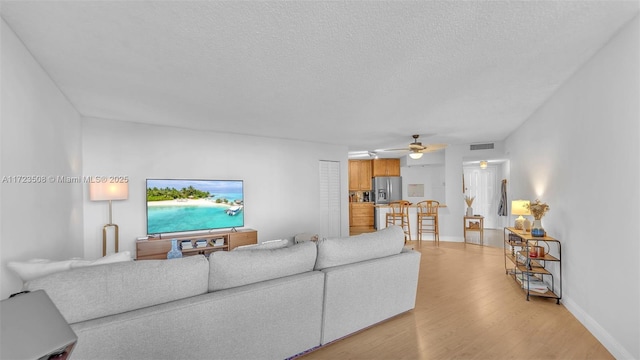 living room with ceiling fan, a textured ceiling, and light wood-type flooring