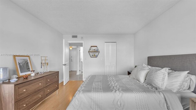 bedroom with a textured ceiling, light hardwood / wood-style flooring, and a closet