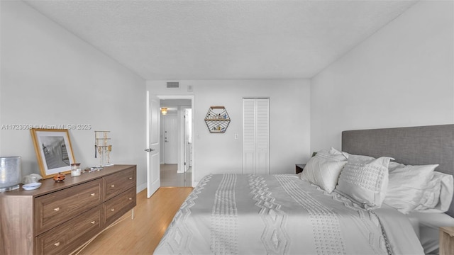 bedroom with light wood-style flooring, visible vents, and a closet