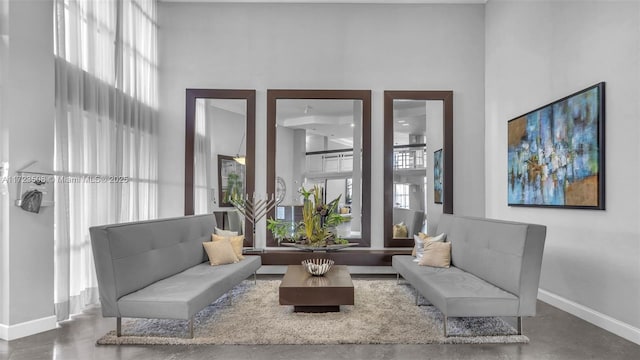 living area featuring baseboards, finished concrete flooring, and a towering ceiling