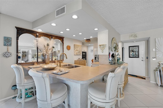 kitchen featuring a breakfast bar, sink, light tile patterned floors, a textured ceiling, and kitchen peninsula