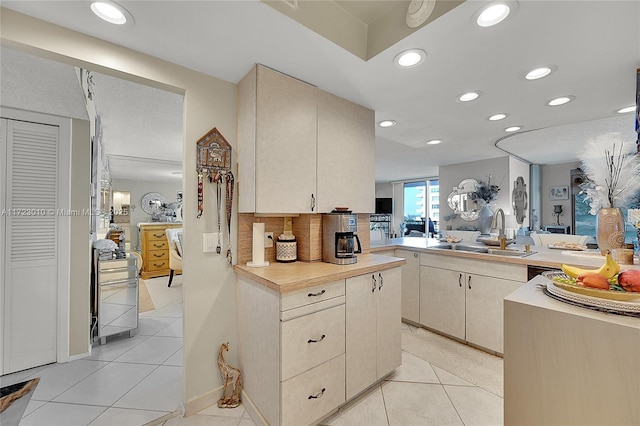 kitchen with sink, tasteful backsplash, kitchen peninsula, cream cabinetry, and light tile patterned flooring