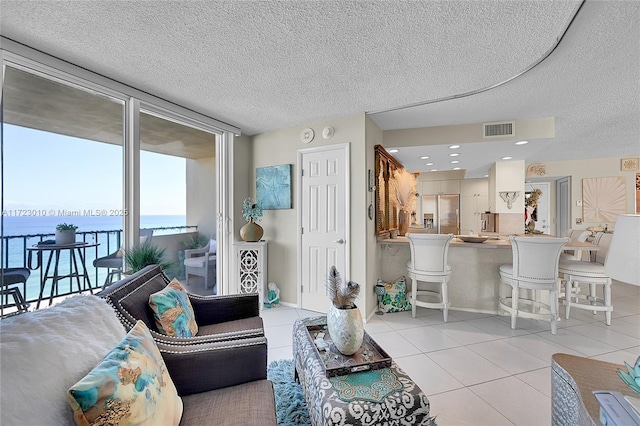 tiled living room featuring expansive windows, a water view, and a textured ceiling