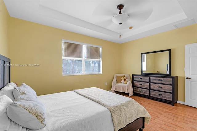 bedroom with hardwood / wood-style flooring, ceiling fan, and a raised ceiling