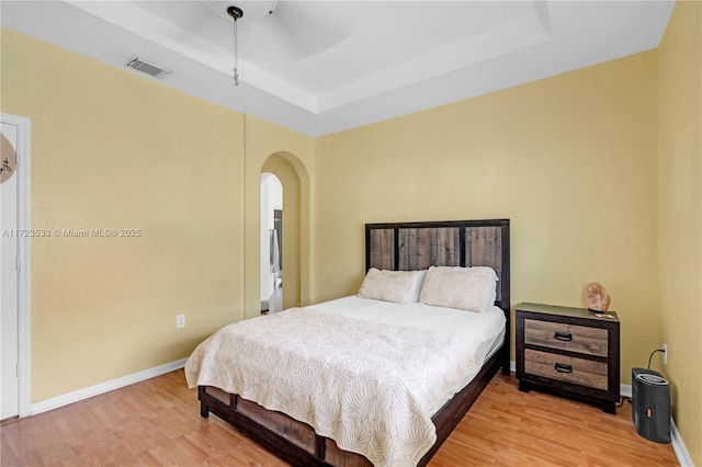 bedroom featuring a raised ceiling, ceiling fan, and light hardwood / wood-style flooring