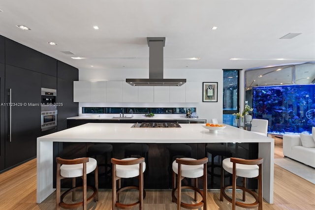 kitchen featuring tasteful backsplash, island range hood, stainless steel gas stovetop, a large island, and oven