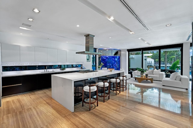 kitchen featuring island range hood, white cabinetry, sink, expansive windows, and a spacious island