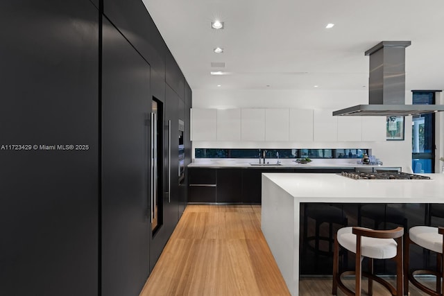 kitchen featuring sink, built in refrigerator, a kitchen breakfast bar, island range hood, and stainless steel gas cooktop