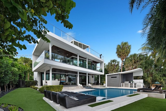 rear view of property featuring a lawn, ceiling fan, a patio, a balcony, and exterior bar