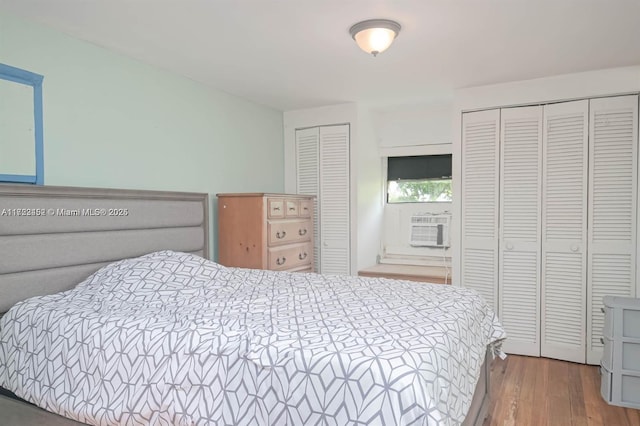 bedroom featuring hardwood / wood-style flooring, cooling unit, and multiple closets