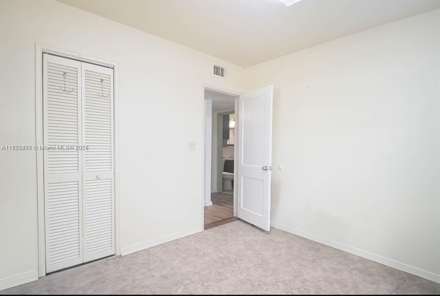 unfurnished bedroom with light colored carpet and a closet