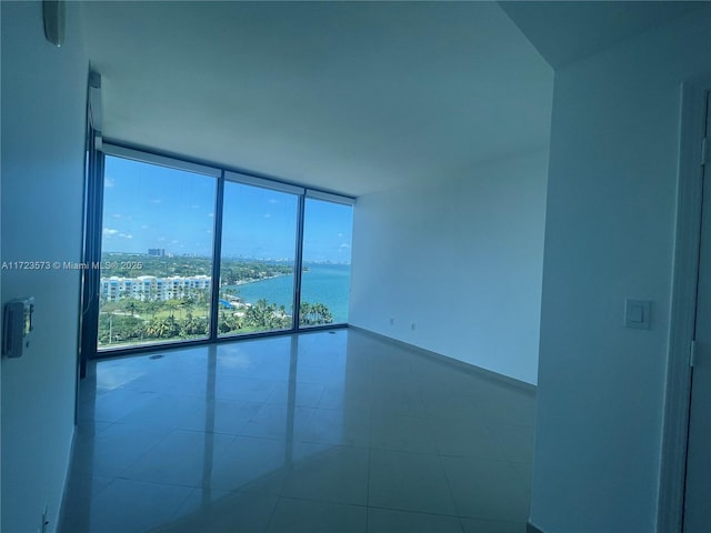 tiled spare room featuring a water view and a wall of windows