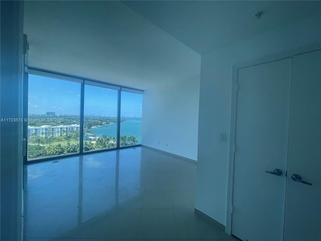 empty room featuring tile patterned flooring, a water view, and floor to ceiling windows