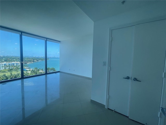 tiled empty room featuring a water view and a wall of windows