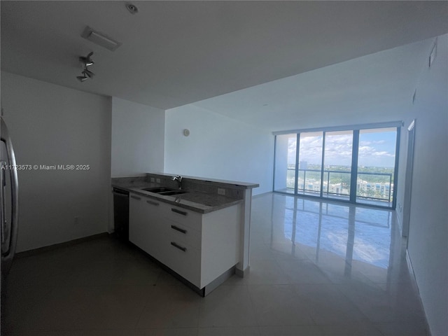 kitchen with kitchen peninsula, stainless steel dishwasher, sink, light tile patterned floors, and white cabinetry