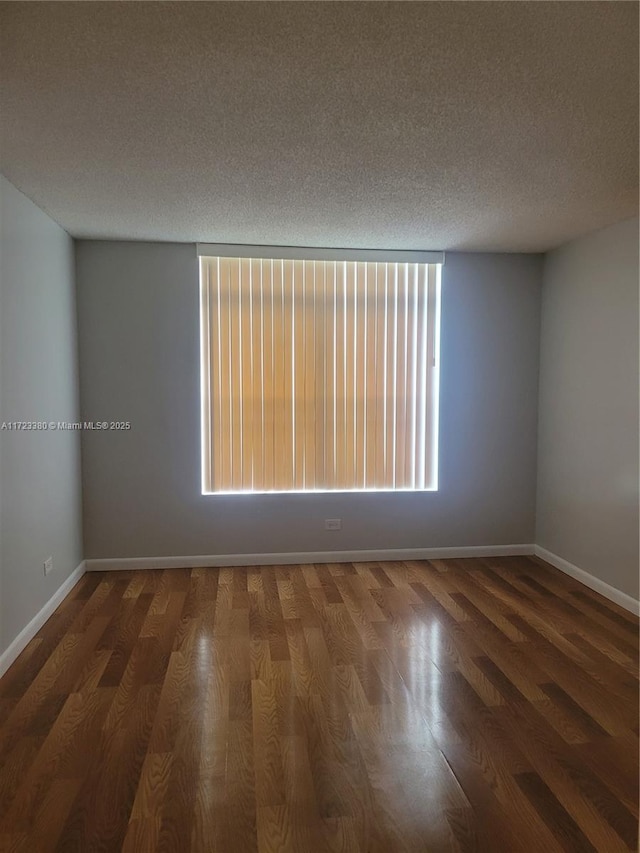 spare room featuring a textured ceiling, dark wood-type flooring, and a healthy amount of sunlight