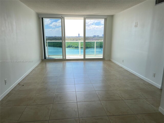 unfurnished room with a wall of windows, a textured ceiling, and light tile patterned floors