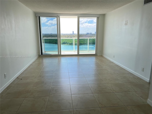 empty room with visible vents, a textured ceiling, tile patterned flooring, a wall of windows, and baseboards