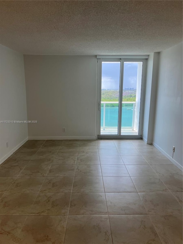 tiled empty room featuring a textured ceiling and baseboards