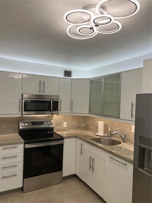 kitchen with sink, stainless steel appliances, tasteful backsplash, light stone counters, and light tile patterned flooring