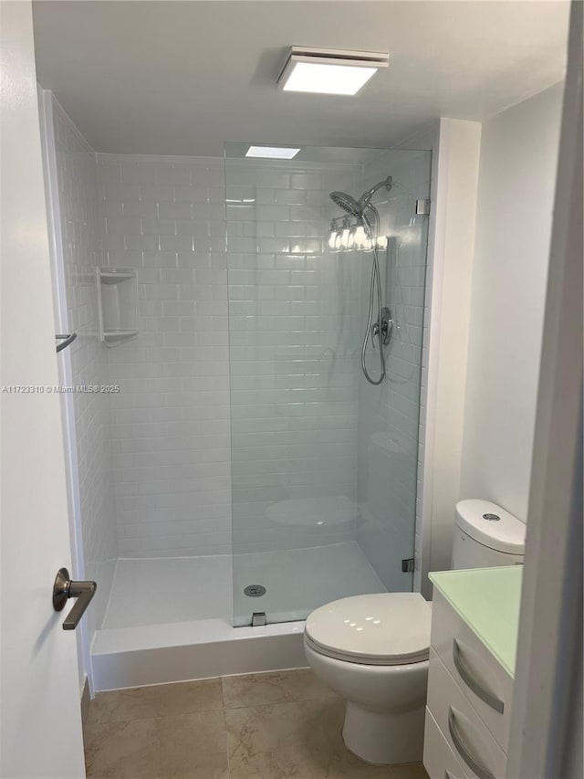 bathroom with toilet, a tile shower, and vanity