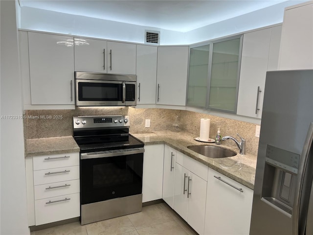 kitchen featuring light stone counters, visible vents, decorative backsplash, appliances with stainless steel finishes, and a sink