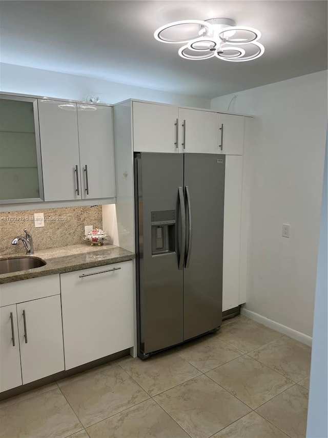 kitchen featuring a sink, white cabinetry, backsplash, stainless steel fridge, and glass insert cabinets