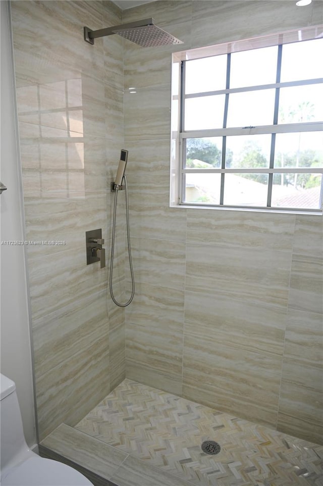 bathroom featuring toilet, a tile shower, and plenty of natural light