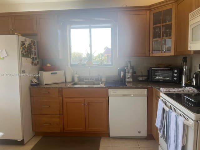 kitchen with tasteful backsplash, white appliances, sink, light tile patterned floors, and dark stone countertops