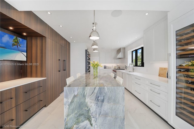 kitchen featuring wall chimney range hood, sink, decorative light fixtures, light stone counters, and white cabinetry