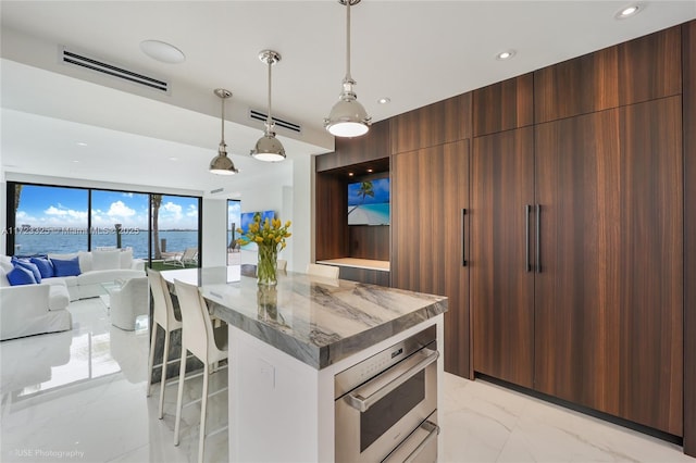 kitchen with a center island, light stone counters, expansive windows, decorative light fixtures, and a water view